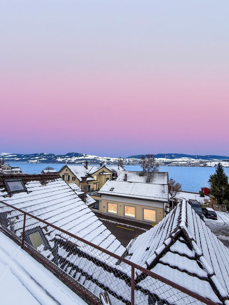 Houses with snow-covered roofs, a lake, and mountains in the background
