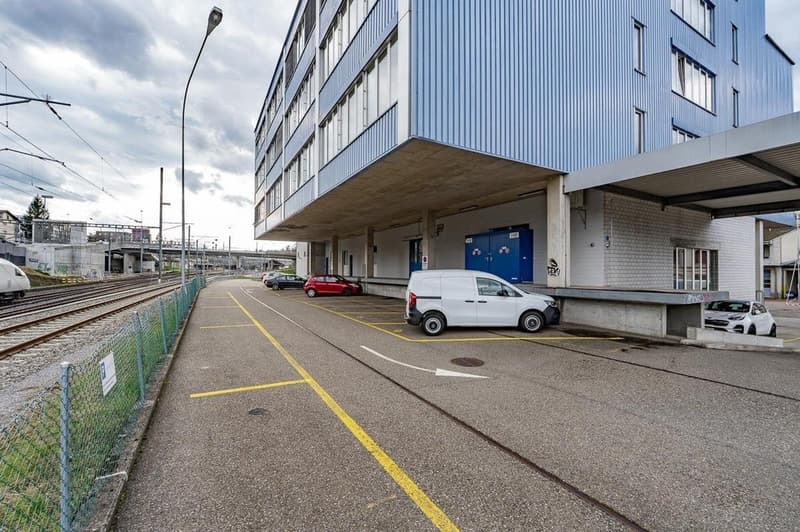 modern blue building with windows, cars parked in front, fenced parking area, street light