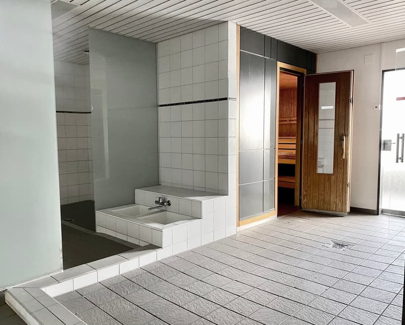 Tiled bathroom with a sauna, sink, and wooden door leading to another room