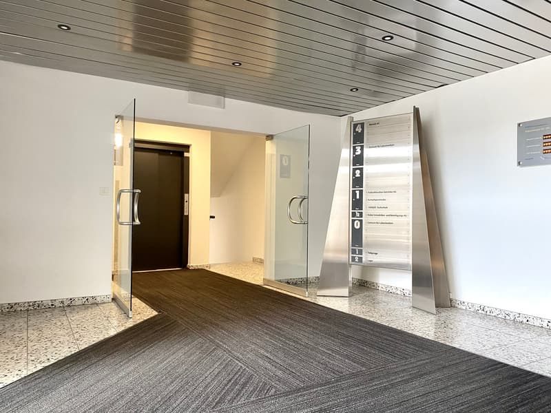 Entrance with glass doors, carpeted floor, metal directory, elevator, and a glass wall.