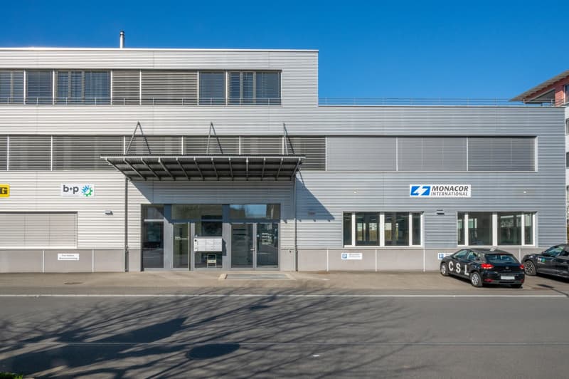 modern two-story office building, large windows, metal walls, entrance with canopy, signage on wall, parking lot with parked cars in front