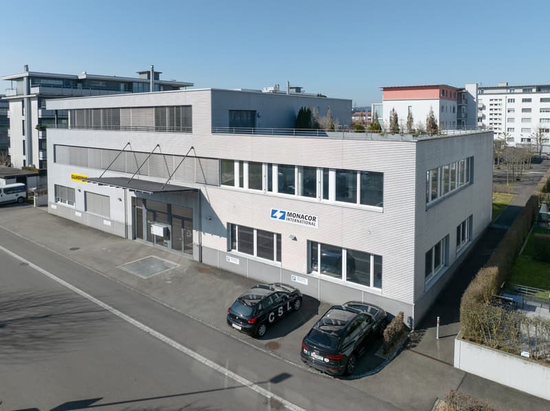 A modern office building with gray walls and white windows, parking lot in front, two cars parked