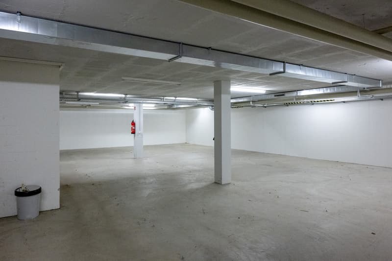 empty parking place, white walls, gray floor, ceiling with metal frames, fire extinguisher, white ceiling with fluorescent lamps