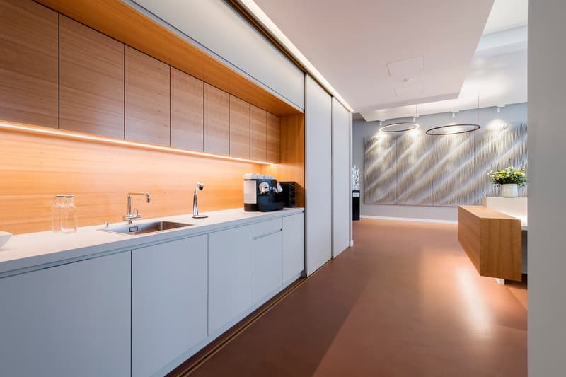 modern kitchen with wooden cabinets, white countertops, stainless steel sink, faucet, coffee machine, and a vase with flowers