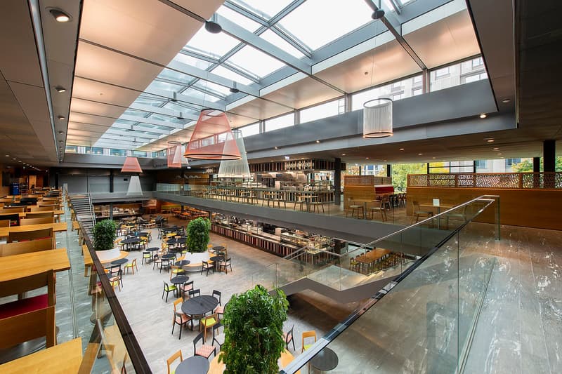 Multi-level indoor dining area with glass railings, tables, chairs, and plants