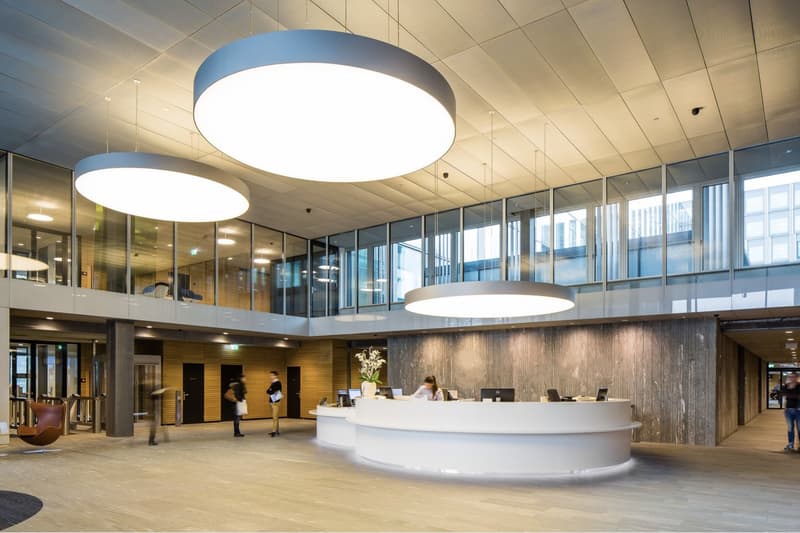 Modern office reception area, large circular lighting fixtures, glass walls, wooden paneling, front desk, large room