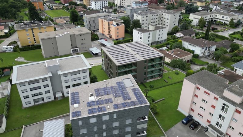 Apartment complex, modern design, multiple buildings, solar panels on rooftops, communal garden area, several cars parked