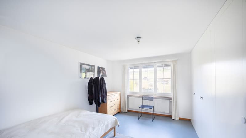 single bed, wooden dresser, chair, radiator, window, picture frames, white walls, ceiling lamp