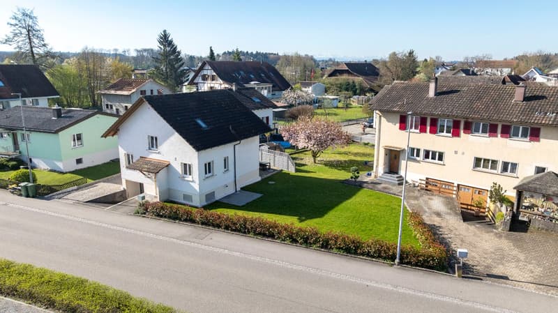 Aerial view of a neighborhood with several houses, one with a garage, surrounded by trees and grass.