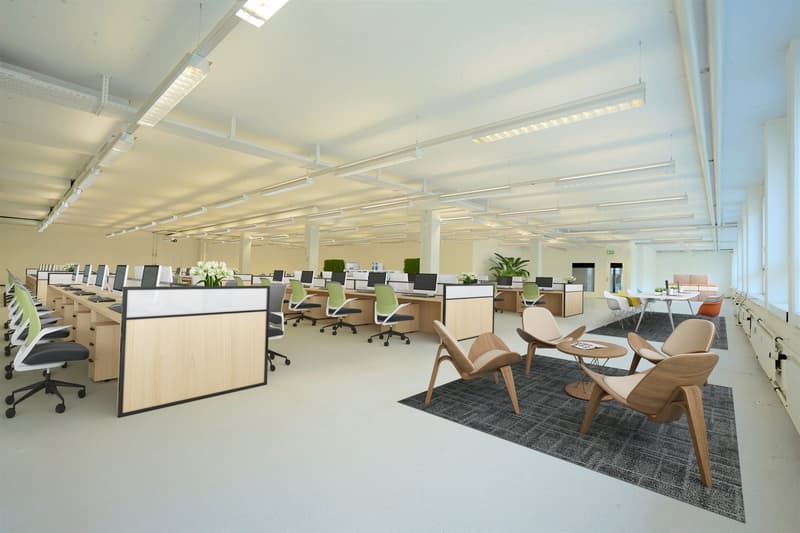 Open floor office with desks, computer monitors, seating areas, chairs, tables, plants