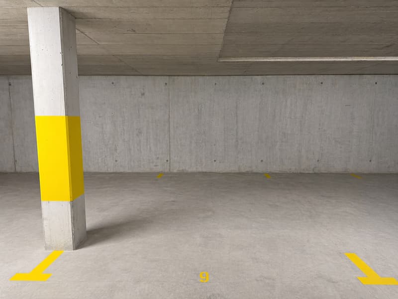 Empty parking lot with concrete walls, yellow markings, and a central column.