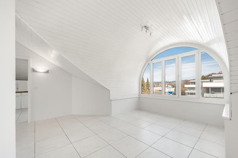 Bright and spacious attic room with arched window, white walls and ceiling, and tiled flooring.