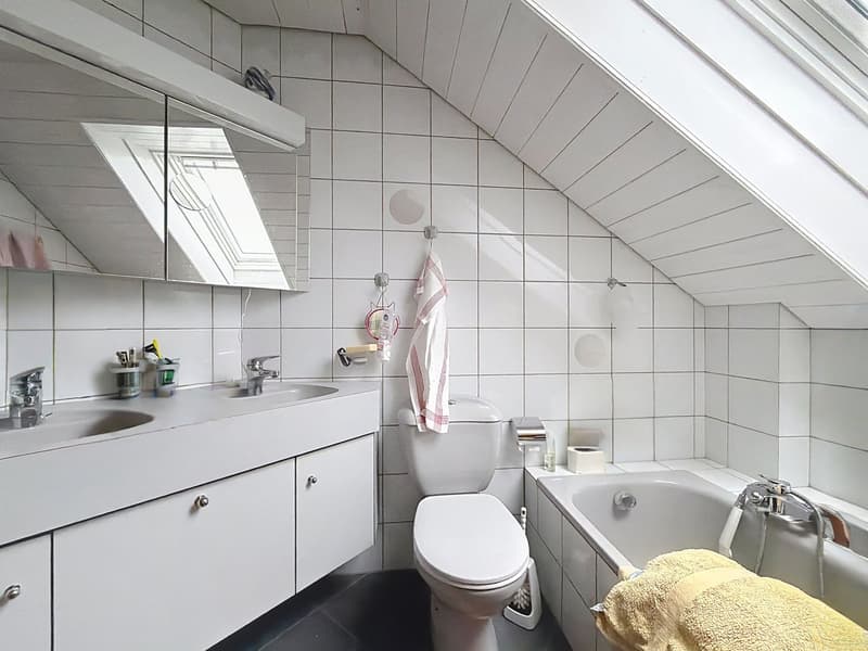 Bathroom with white tiles, white sink, white toilet, bathtub, mirror, towel, and towel rack.