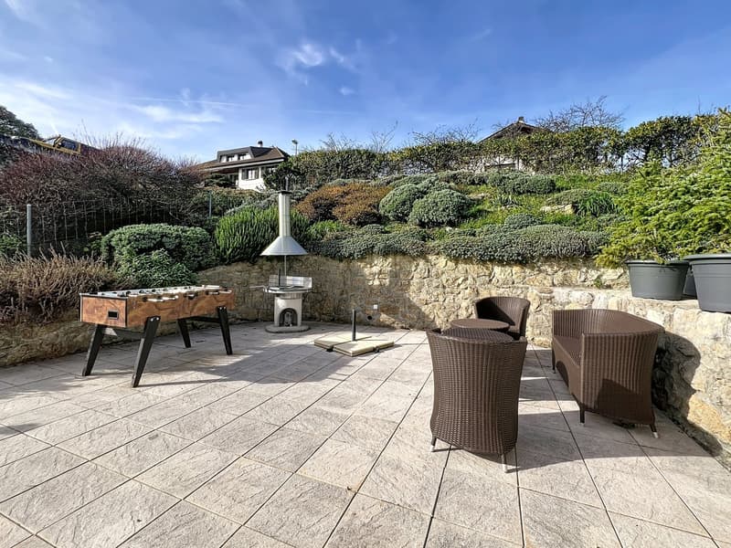 Outdoor patio with stone wall, foosball table, outdoor seating, stone flooring, greenery, and a small outdoor fireplace.