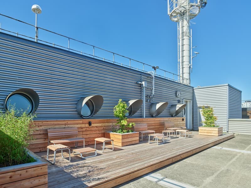 Wooden deck, metal railing, circular windows, wooden benches, potted plants, street light