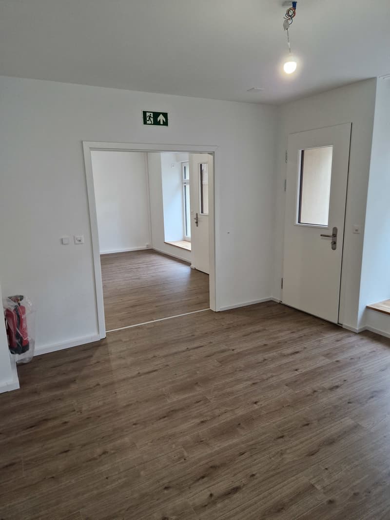empty room, wooden floor, white walls, two doors, one with a window, emergency exit sign