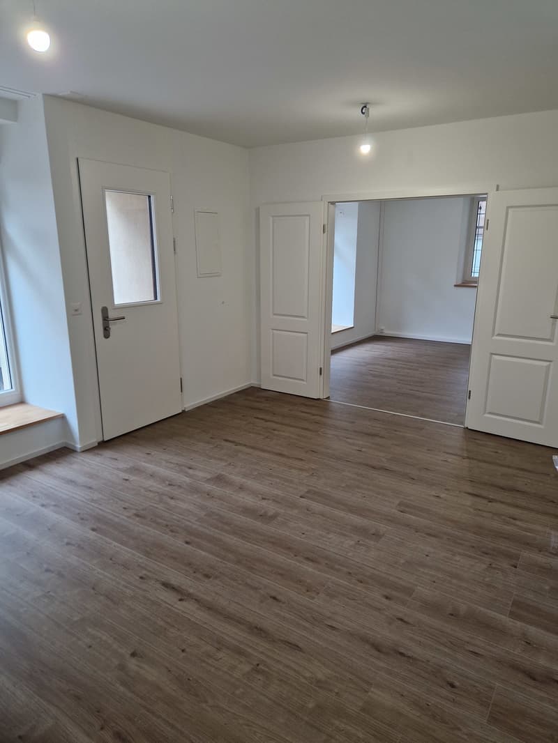 Empty room with wooden floors, white walls, three doors, and windows