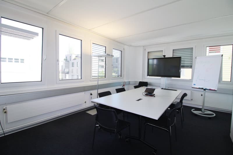 white walls, black carpet, white table, black chairs, windows, radiators, whiteboard, monitor