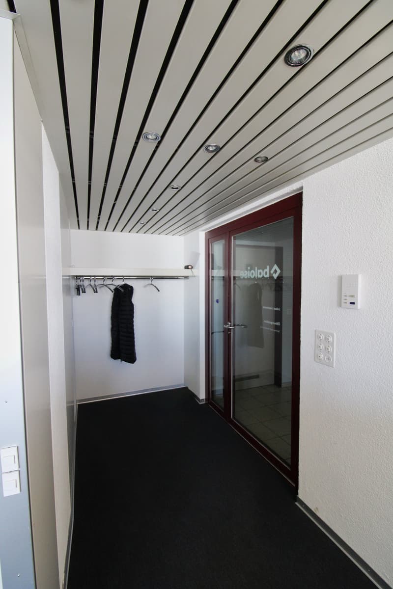 Empty room with white walls, black carpet, glass door, and a small closet with a rack of hangers