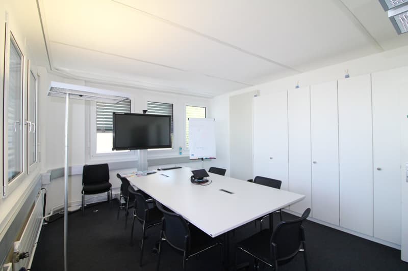 conference room with a long white table, black chairs, a whiteboard, a flat screen TV, and white cabinets