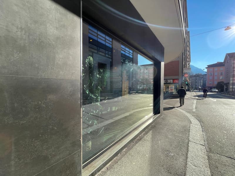 modern building with large glass windows, gray exterior wall, sidewalk, street with people walking
