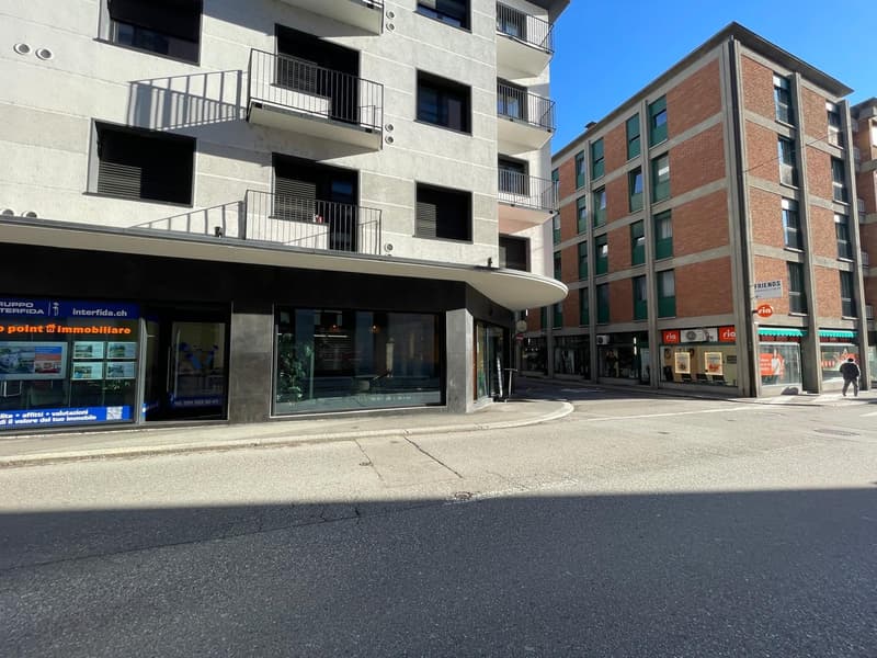 Modern apartment building with glass windows, balconies, and a commercial space on the ground floor.