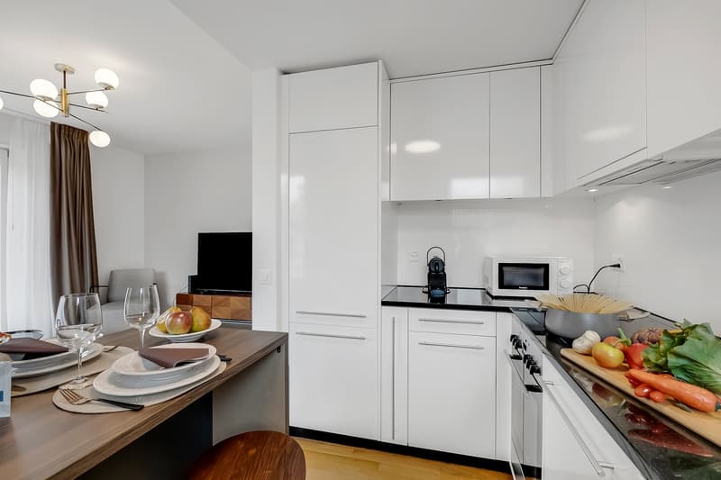 modern kitchen with dining area, white cabinets, black countertops, modern appliances, wooden dining table, modern chandelier