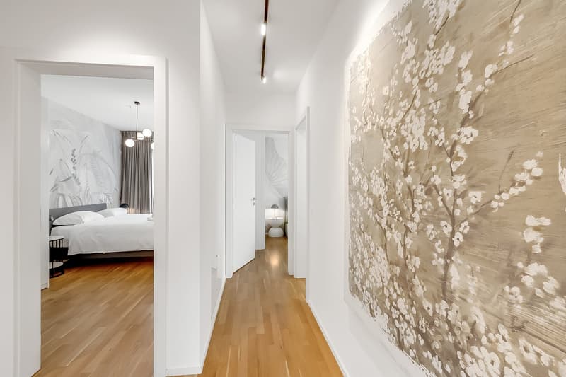 wooden floor, white walls, large painting, hallway, bedroom with bed and pillows, mirror, lamp