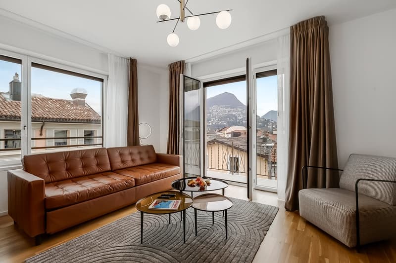 modern living room with a brown leather sofa, a glass coffee table, a rug, and a balcony with a view of the city