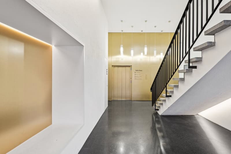 modern hallway, white walls, black floor, gold accent wall, elevator, stairs