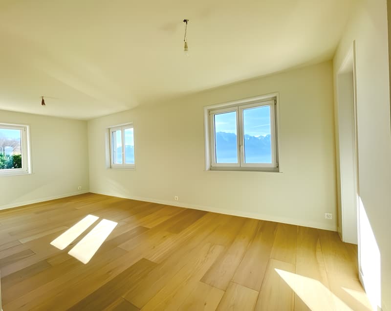 Spacious room with large windows offering a scenic view, hardwood flooring, and neutral-colored walls.