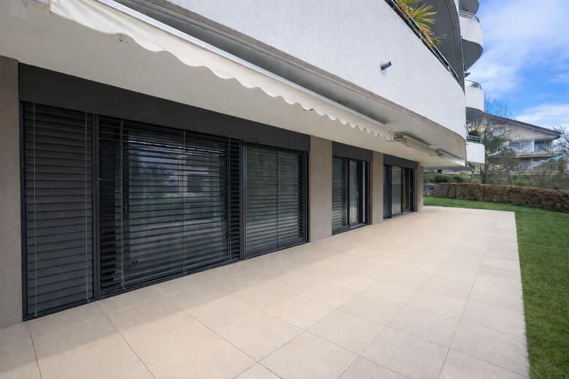 Modern building with tiled entrance, awning, black shutters, and a balcony with railings