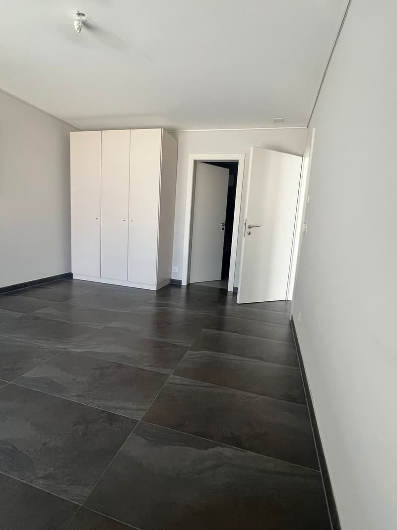 Empty room with white walls, tiled floor, two white doors, and a white wardrobe.