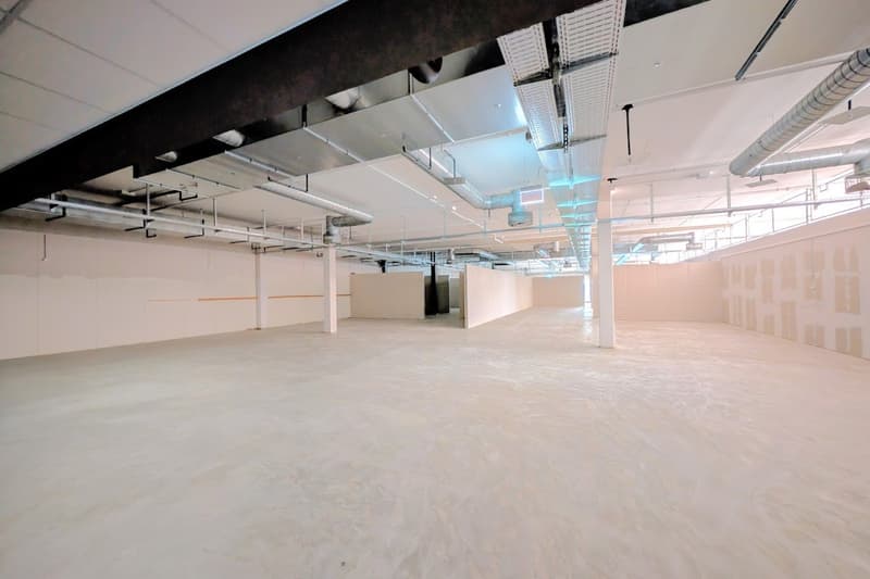 Large empty room, bare walls, concrete floor, exposed ducts, unfinished ceiling