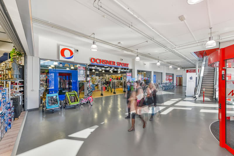 Ochmsner Sport store, bright and spacious mall, escalators, people shopping, bicycles on display, products and shelves.