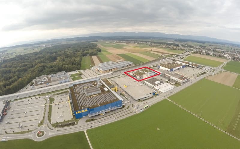 Aerial view of IKEA store surrounded by several buildings, trees, and parking lots. Wide green fields surround the store.