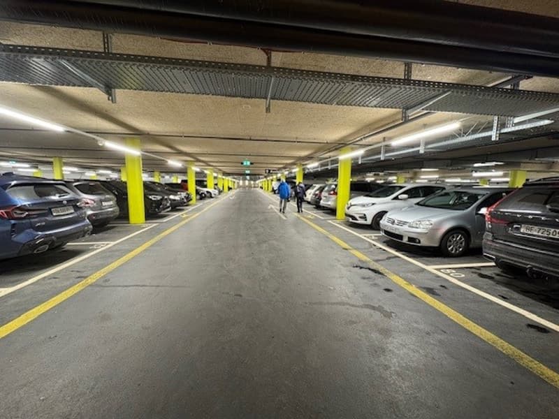 underground parking lot with yellow pillars, cars parked on both sides, two people walking in the middle
