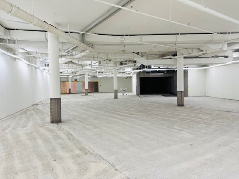 Empty room with white walls, concrete floor, metal beams, and pipes on the ceiling