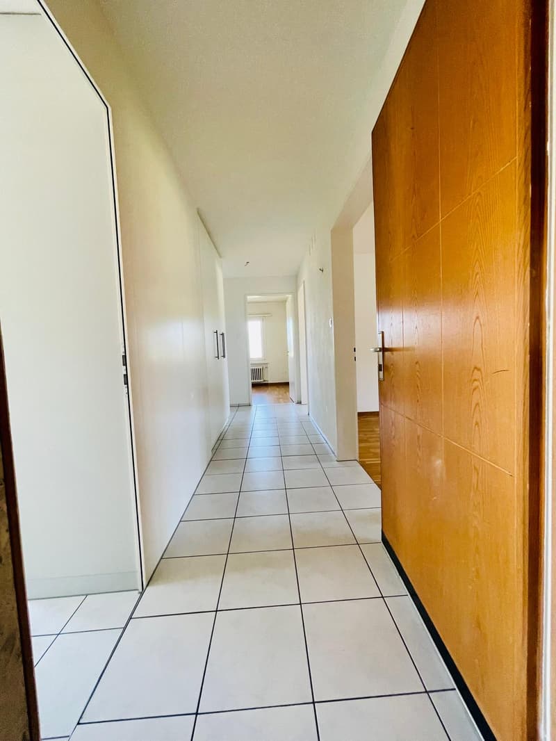 White tiled floor, white walls, wooden door, hallway leading to rooms