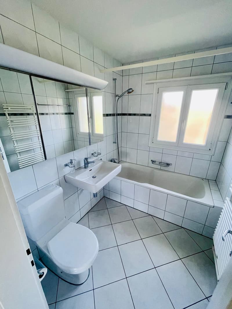 Bathroom with white tiles, bathtub, sink, toilet, mirror, and towel rack