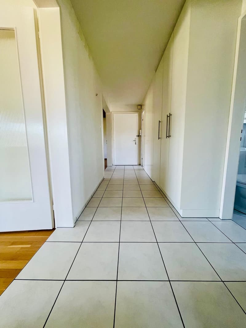 Empty hallway with white tiles, white walls, wooden floor, white doors, and built-in cabinets.
