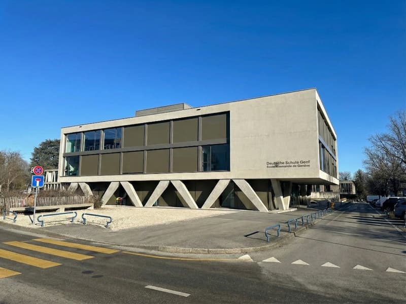 Modern building with glass windows, concrete structure, triangular design, and a sign reading 'Deutsche Schule Genf'.