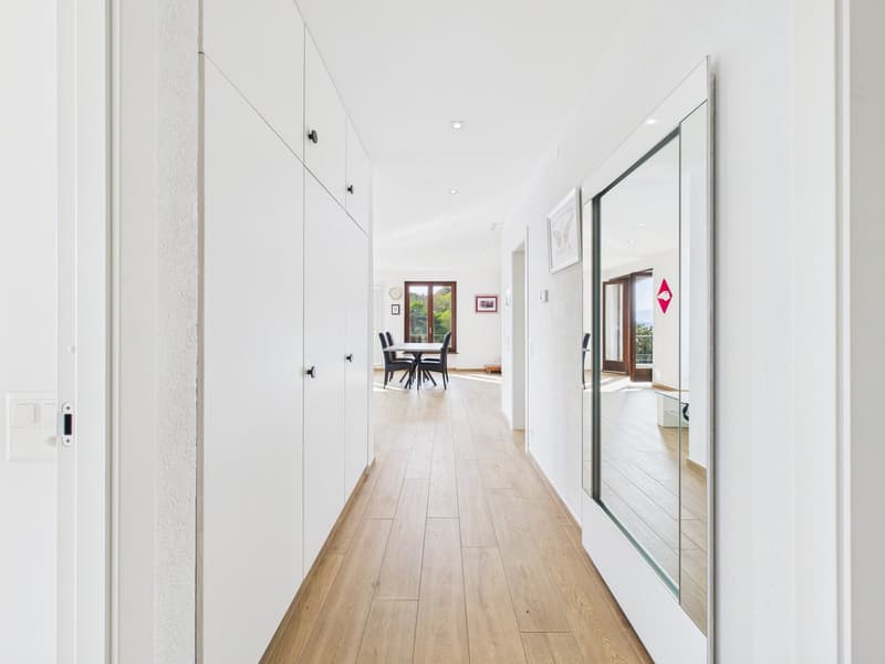 long hallway, wooden floor, white walls, large mirror, dining table and chairs in the distance