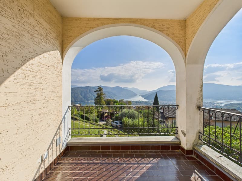 Balcony with arched entrance, tiled floor, metal railing, view of mountains and lake