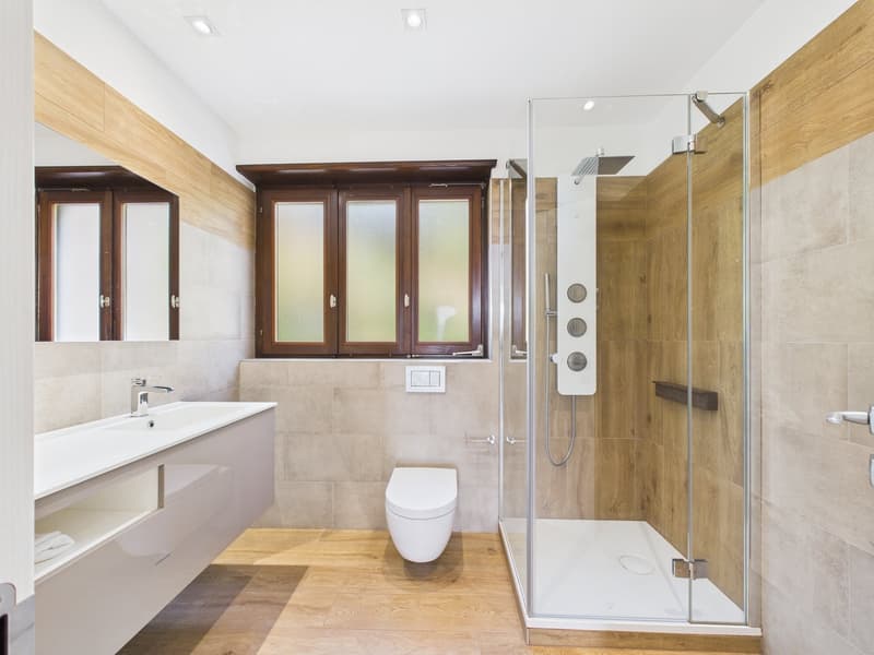 modern bathroom with wooden floor, white sink, white toilet, glass shower enclosure, wooden wall panels, white tiles