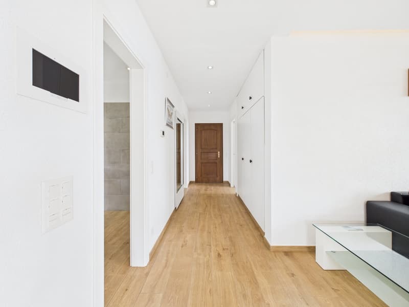Empty hallway with wooden floors, white walls, and a glass table on the right side.