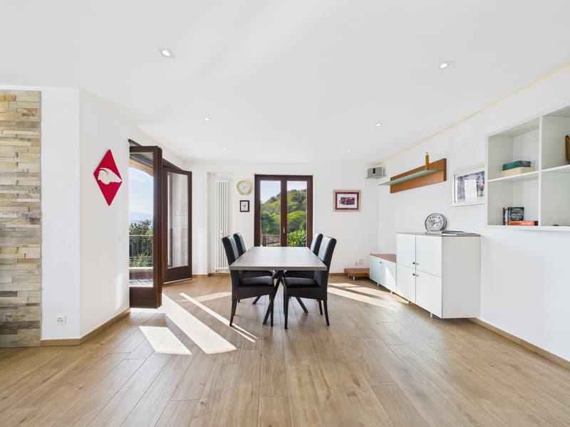 Dining room with wooden floor, white walls, dining table, black chairs, open doors to balcony, shelves, radiator, picture frames, clock, books, plate, and decorative items