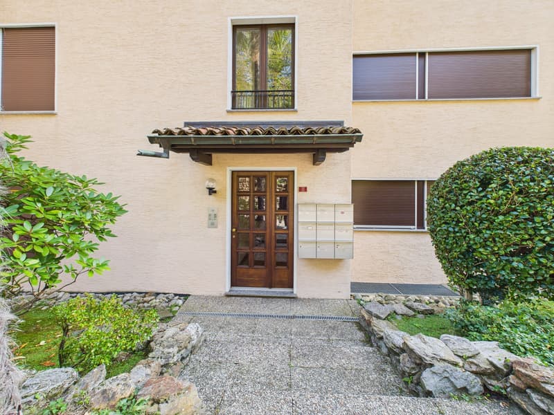 Facade of a beige building with wooden door, mailbox, and small garden in front