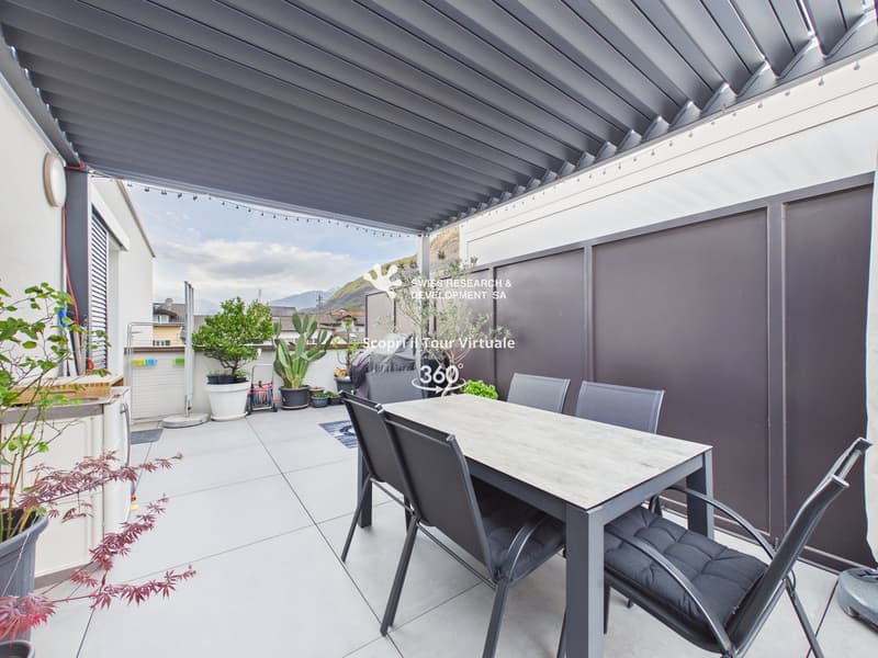 Outdoor dining area with a table and chairs, covered by a retractable roof, surrounded by potted plants and greenery.