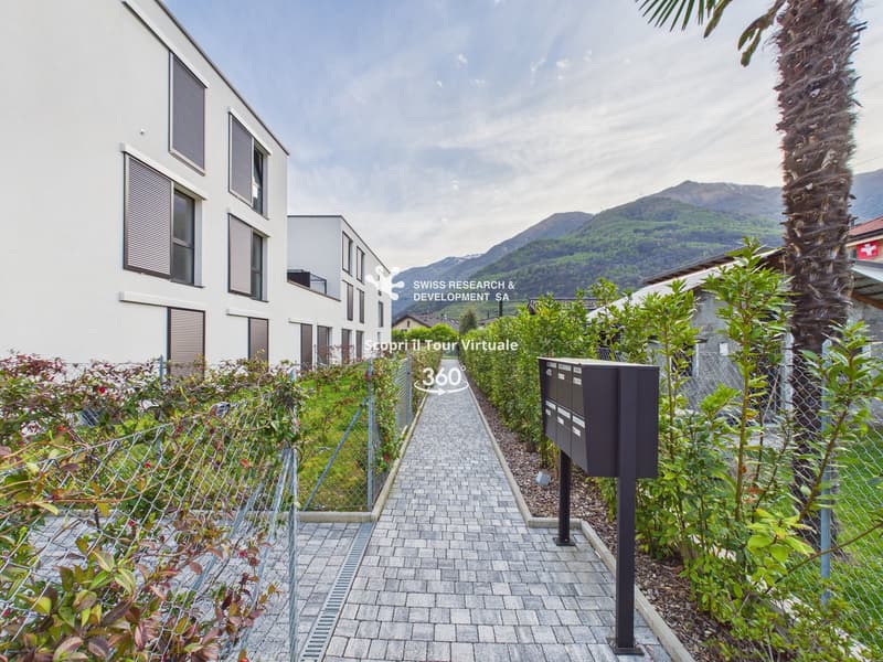 Modern apartment building with white exterior, brick walkway, and greenery.